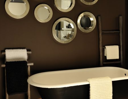 In braun gehaltenes Badezimmer mit runden Spiegel an der braunen Wand und freistehende Badewanne.